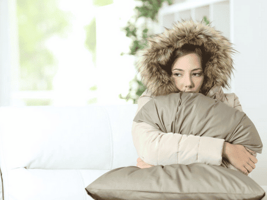 woman wearing winter coat inside because heater is broken